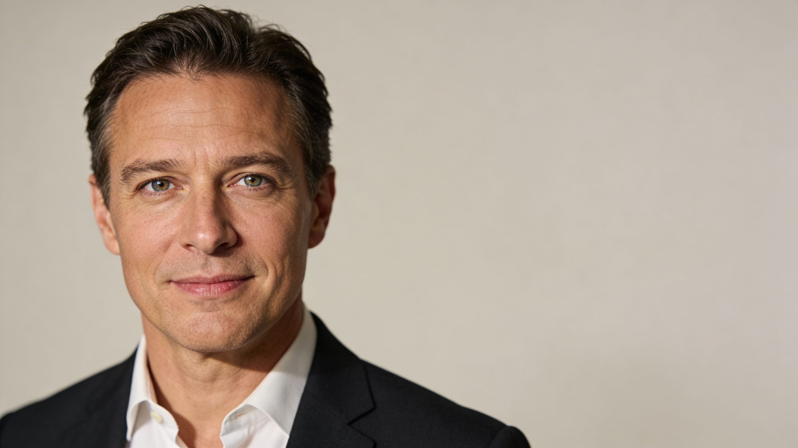 A professional portrait of a man in a black suit and white shirt against a neutral background.