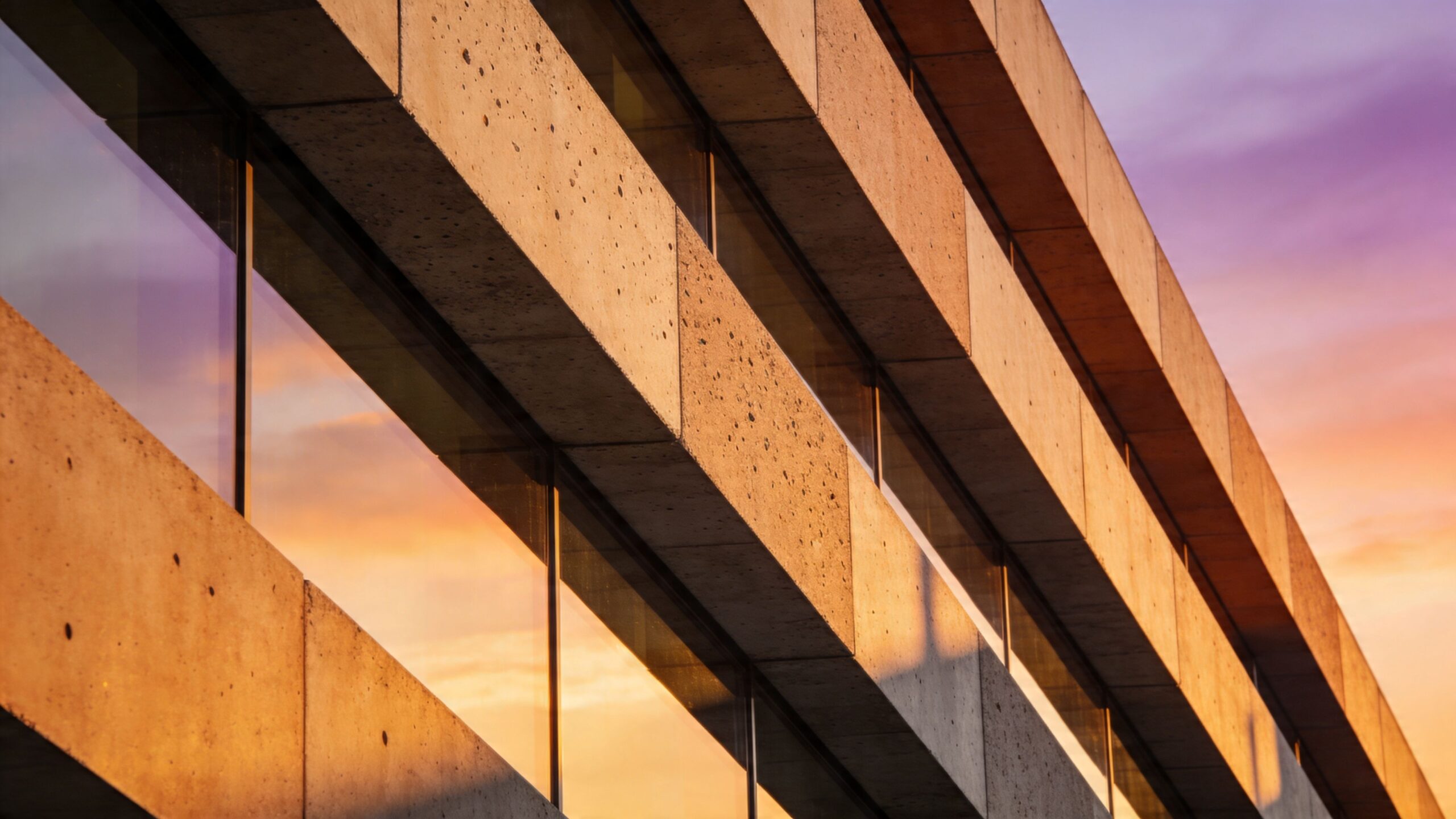 Low angle view of modern concrete building facade reflecting a vibrant sunset in the glass windows.