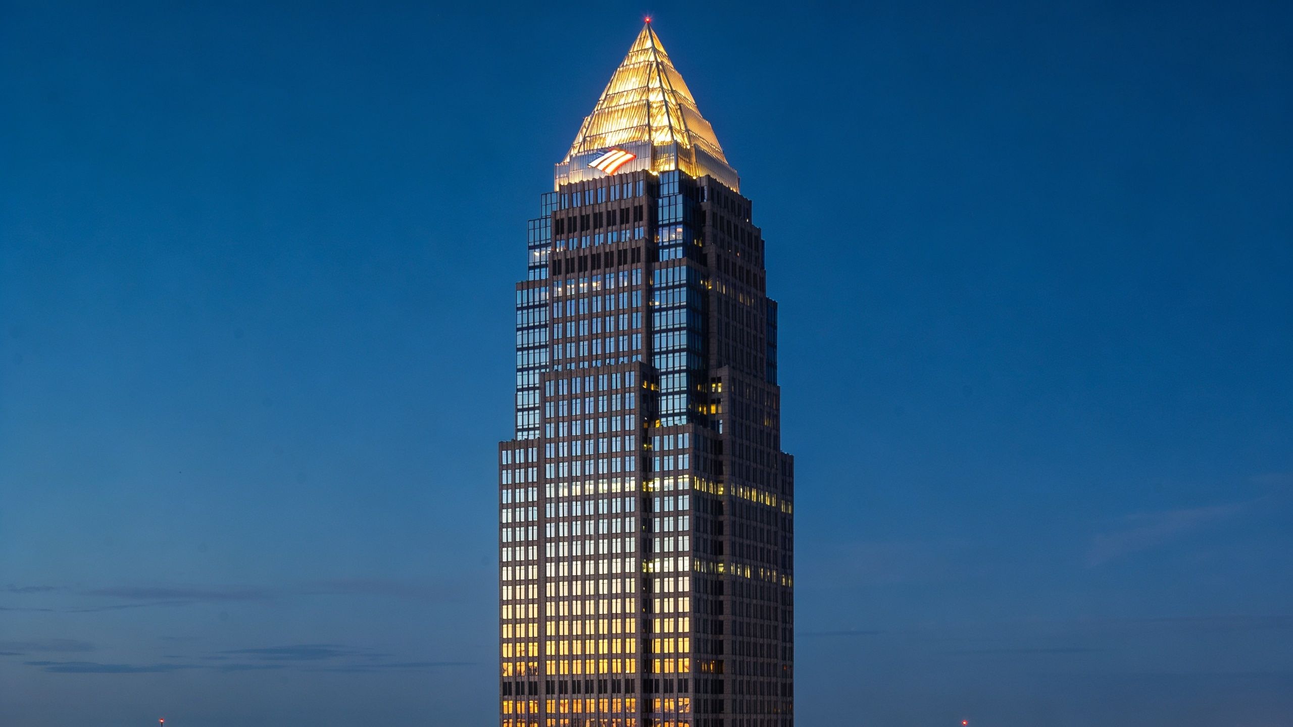 A towering skyscraper featuring a lit pyramidal crown against a clear dark blue twilight sky.