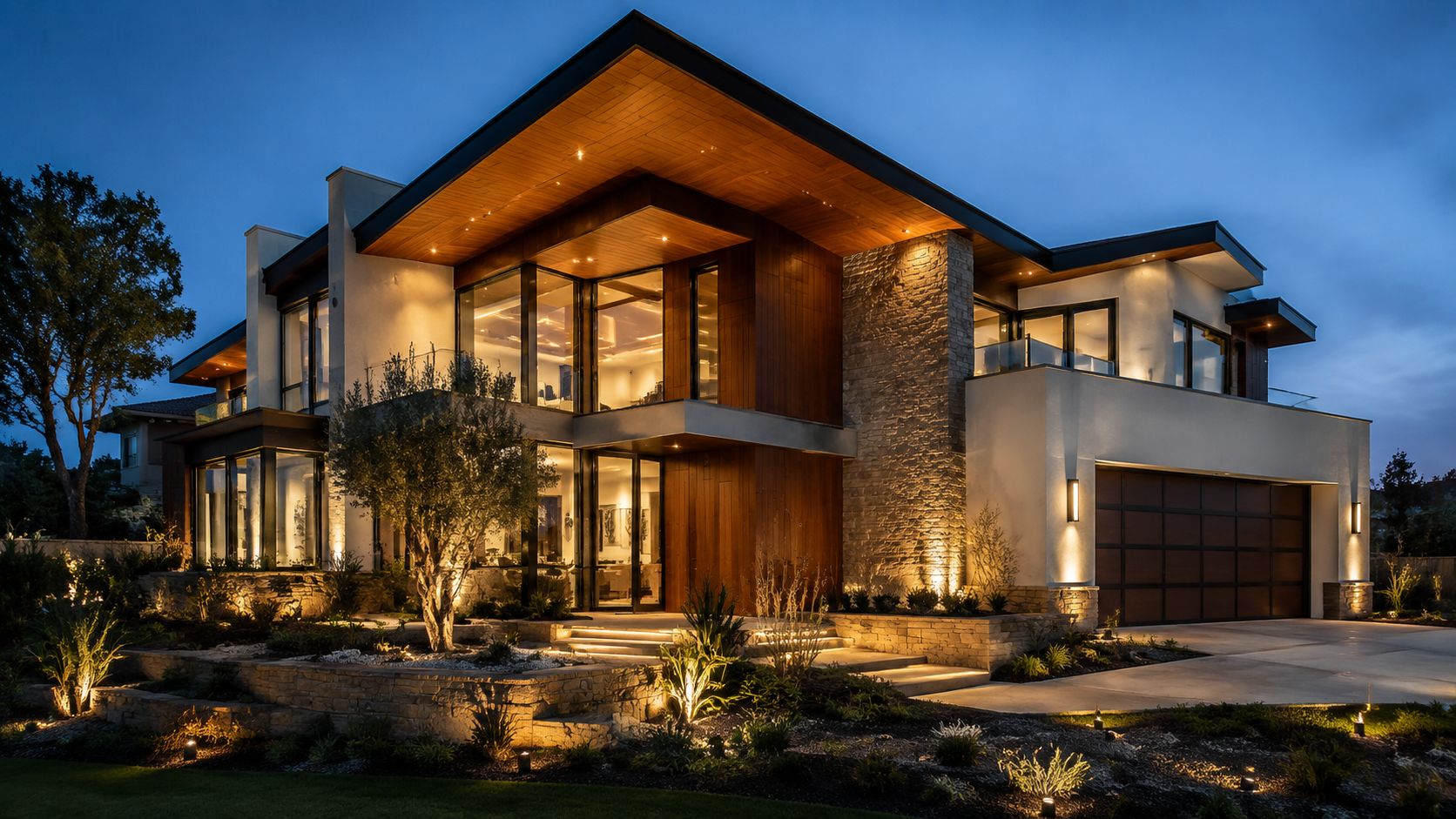 A modern two-story luxury home at twilight featuring warm architectural lighting and beautifully landscaped terraced gardens.