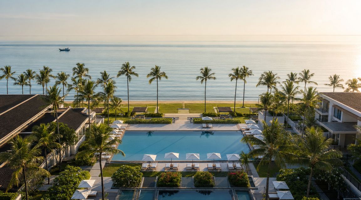 A high-angle drone view of a luxurious beachside resort with a large swimming pool and palm trees.