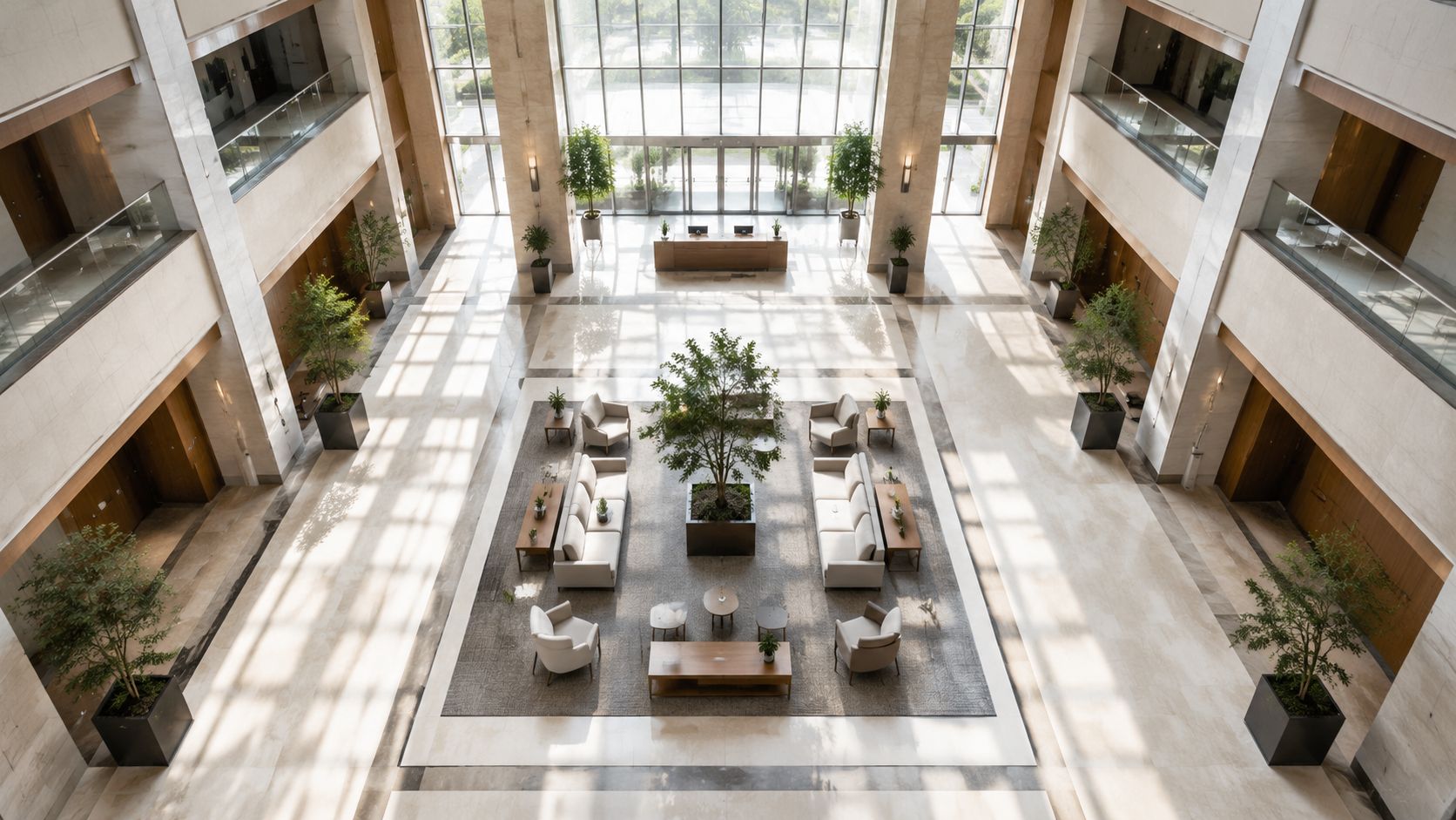An aerial view of a bright hotel lobby featuring modern seating, indoor trees, and tall windows.