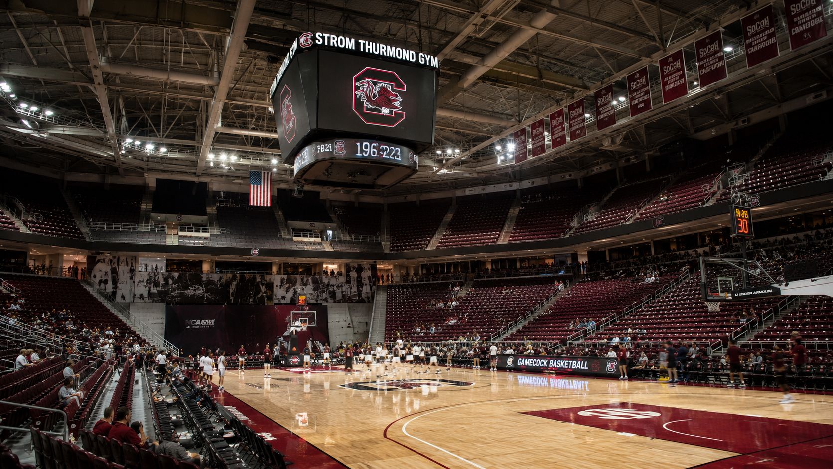 The interior of the Strom Thurmond Gym with a basketball court, bleachers, and a large central scoreboard.