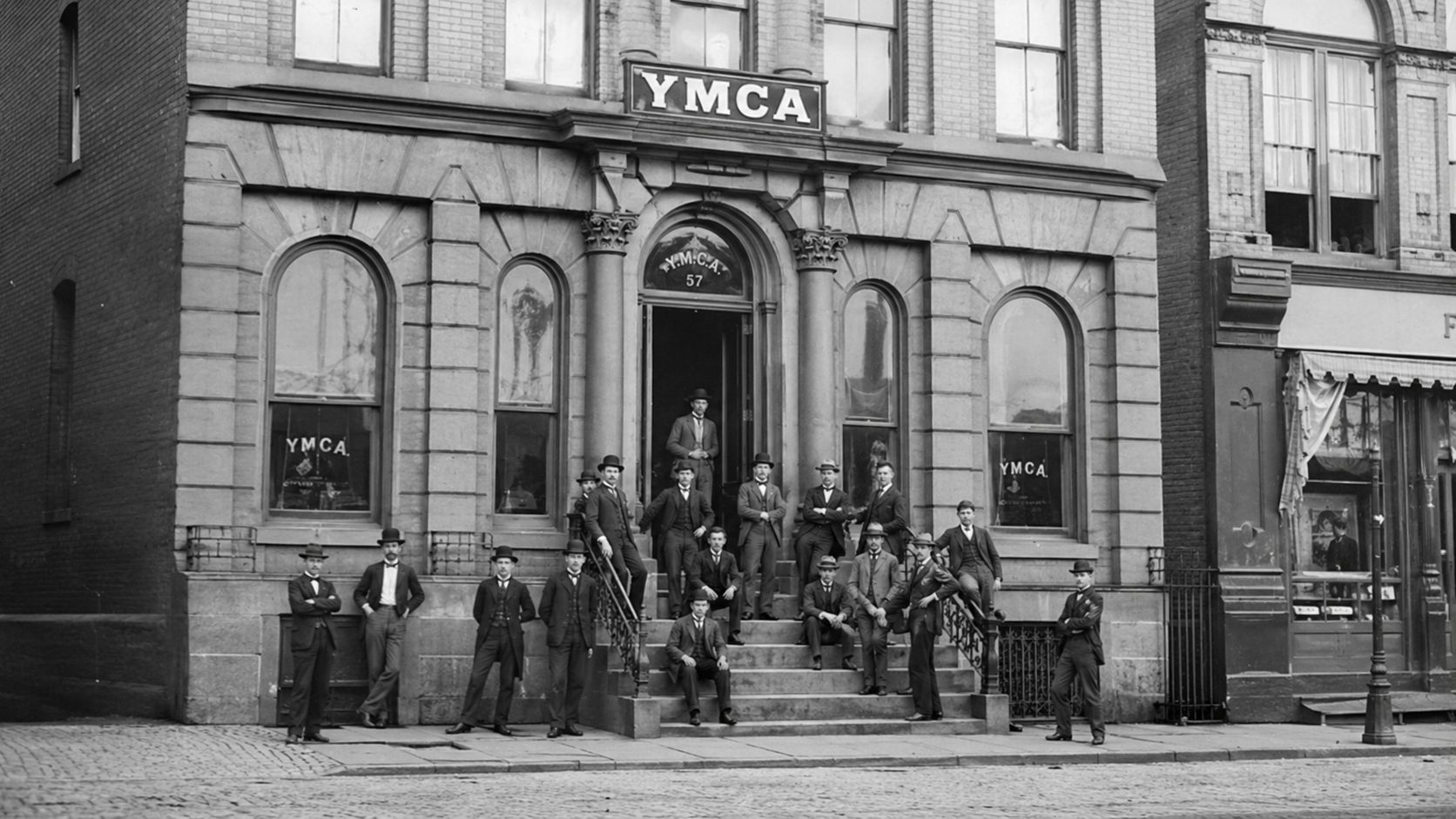 A group of men in suits and hats standing on the stone steps of a YMCA building.