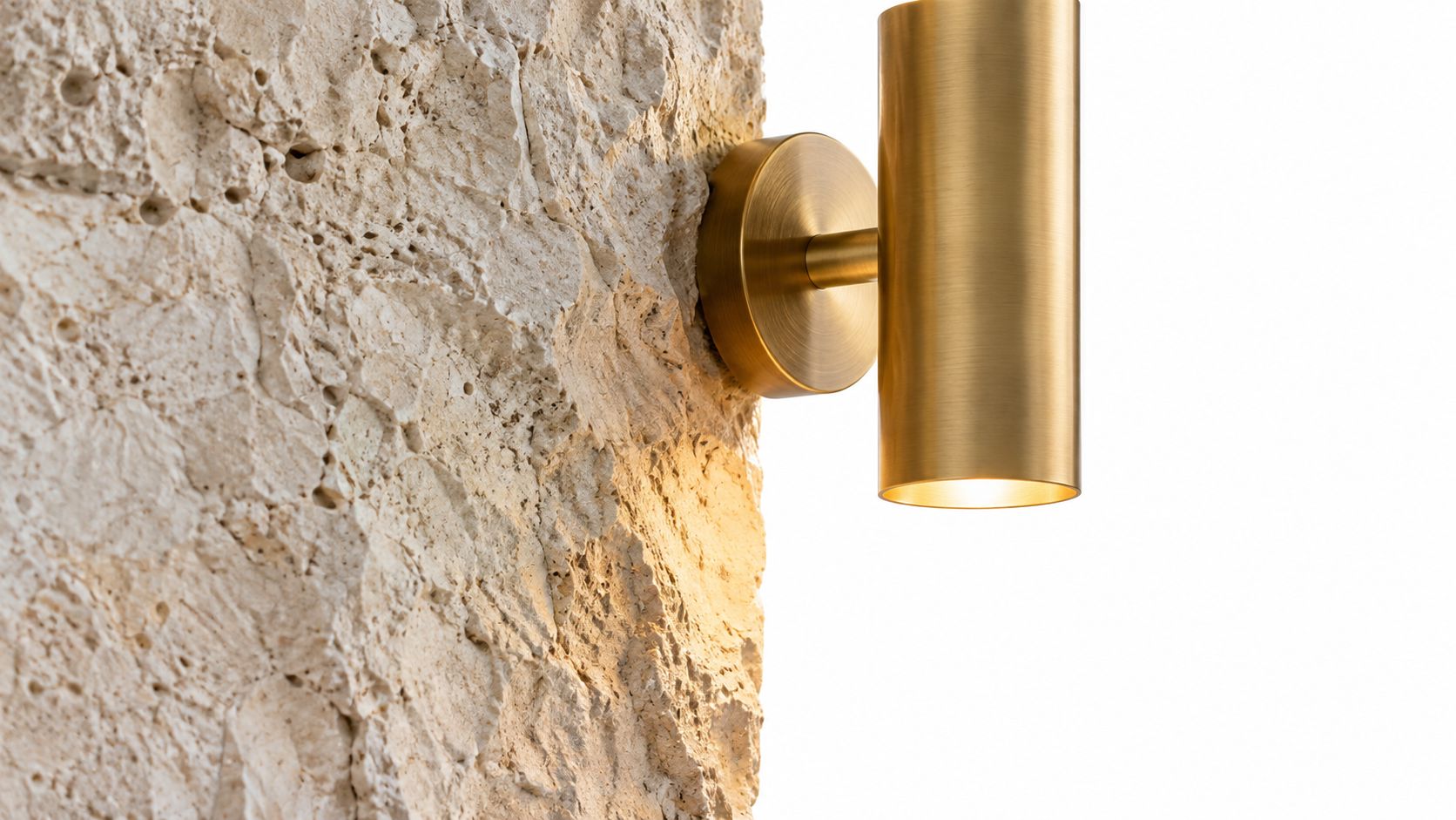 A modern cylindrical gold brass wall light fixture mounted on a rough textured natural stone wall.