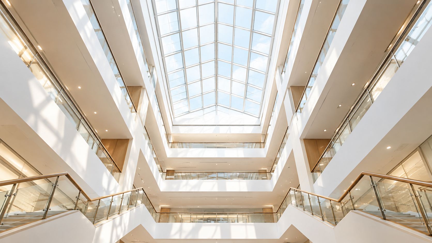 A bright and minimalist interior view of a modern building with a high glass atrium ceiling.
