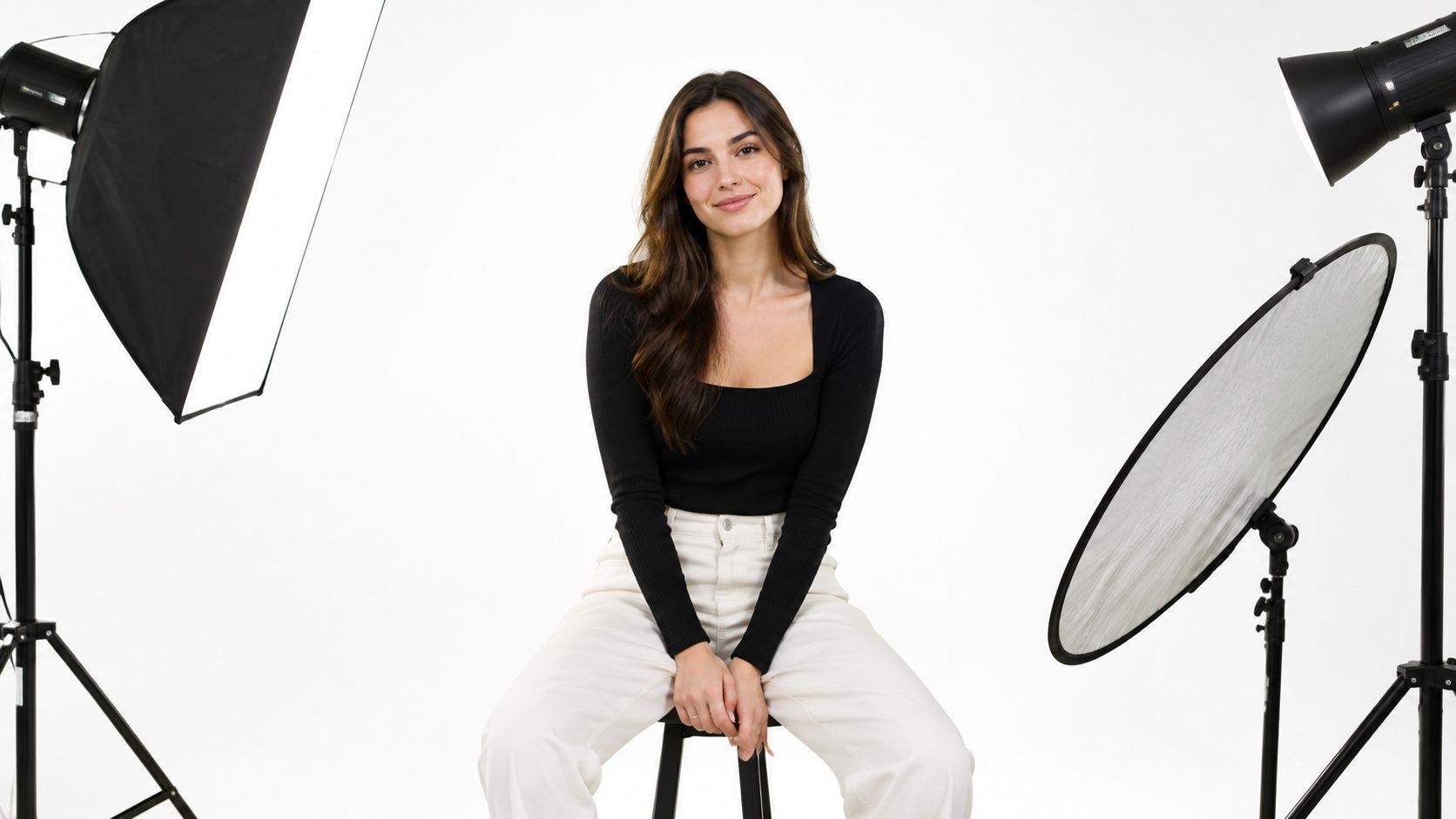 A professional portrait of a woman sitting on a studio stool surrounded by photography lighting equipment